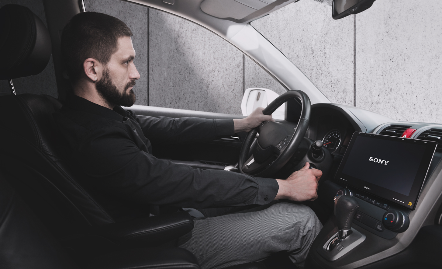 Obrázok osoby, ktorá otáča kľúčom v zapaľovaní, XAV-9550ES v palubnej doske a na obrazovke logo Sony